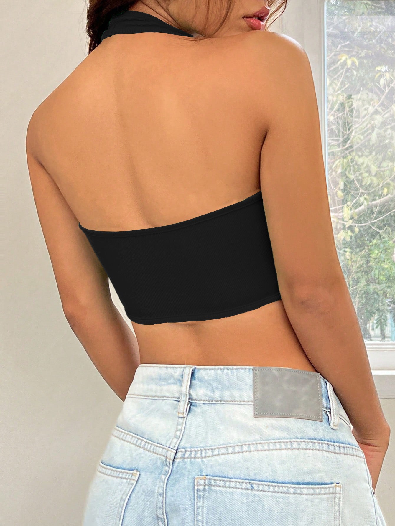 Back view of black ribbed halter crop top with contour seams, paired with light wash denim