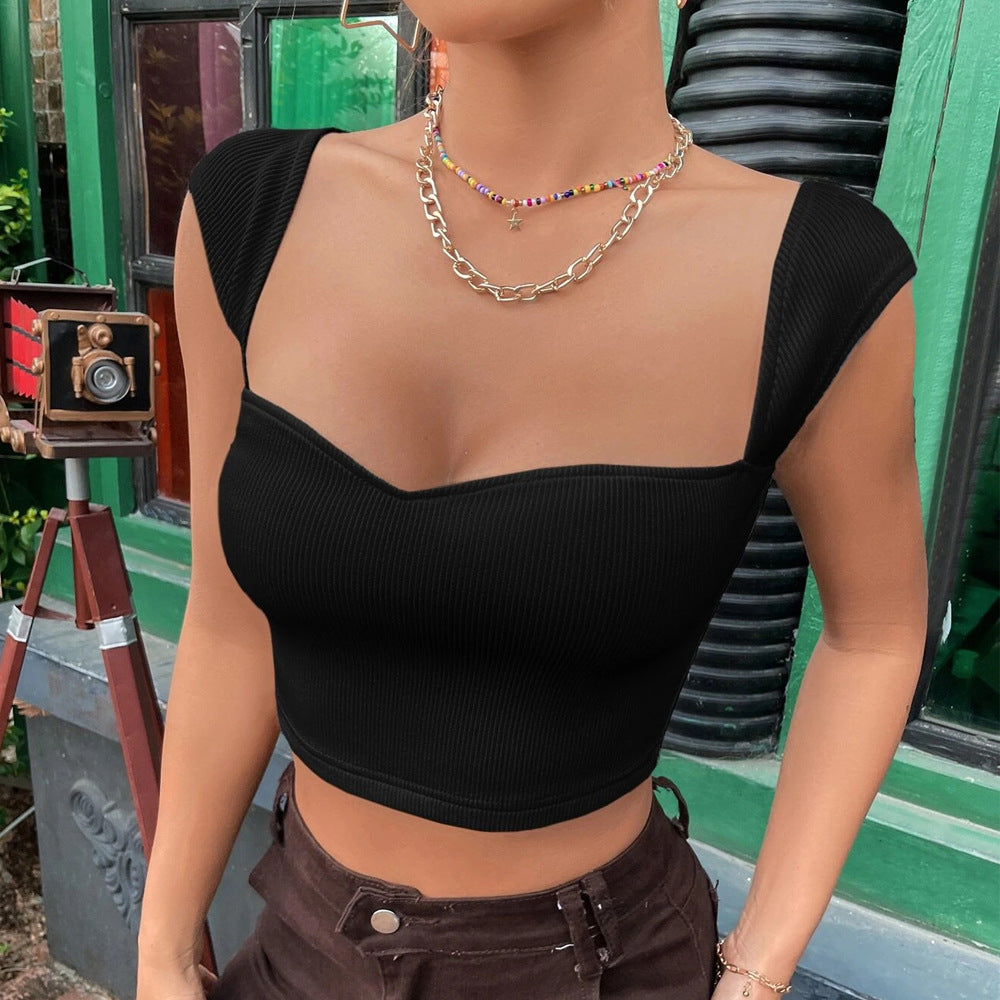 Woman wearing a black ribbed crop top with cap sleeves and a sweetheart neckline, styled with brown pants and layered jewelry