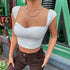 Woman wearing a white ribbed crop top with cap sleeves and a sweetheart neckline, paired with brown pants and layered necklaces