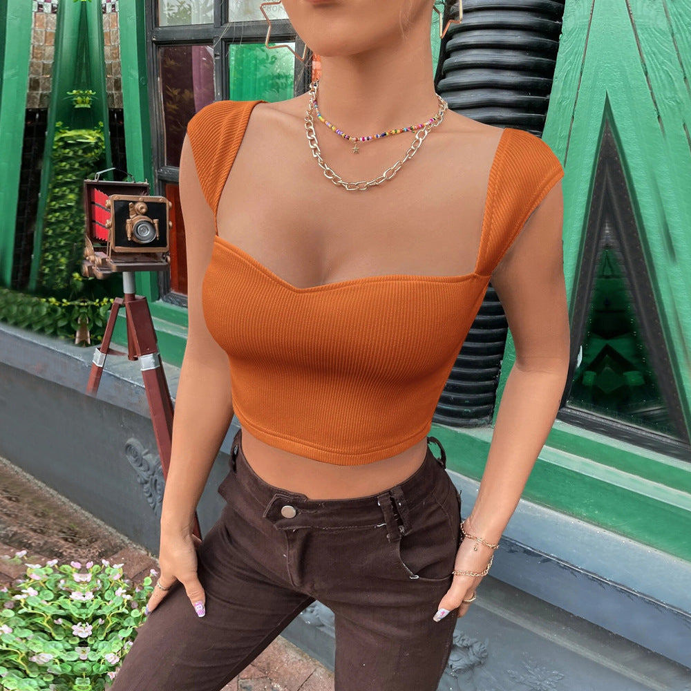 Woman in an orange ribbed crop top with a sweetheart neckline and cap sleeves, styled with brown pants and layered necklaces