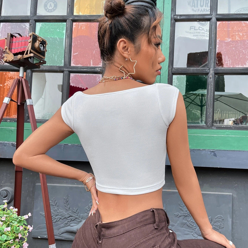 Back view of a woman in a white ribbed crop top with cap sleeves and a scooped back, styled with brown pants and gold accessories