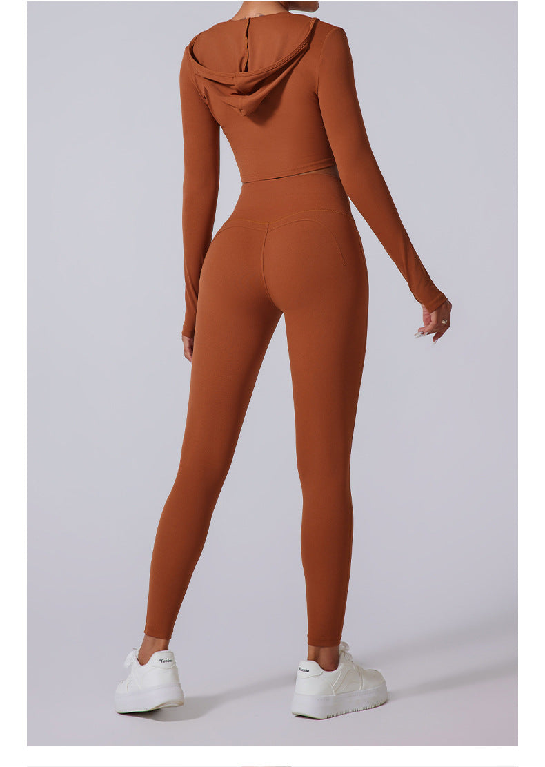 Rear view of model wearing caramel brown workout set with hoodie crop top. High-waisted leggings with contoured seams and white platform sneakers