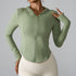 A woman is wearing a sage green zip-up fitness hoodie with thumb holes, gesturing with one hand against gray background