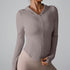 A woman is wearing a taupe fitted workout hoodie with front zipper, posed with hand touching hem against gray background