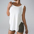 A woman is wearing a white sleeveless tank top with curved hem and olive shorts, touching her collar against a gray background