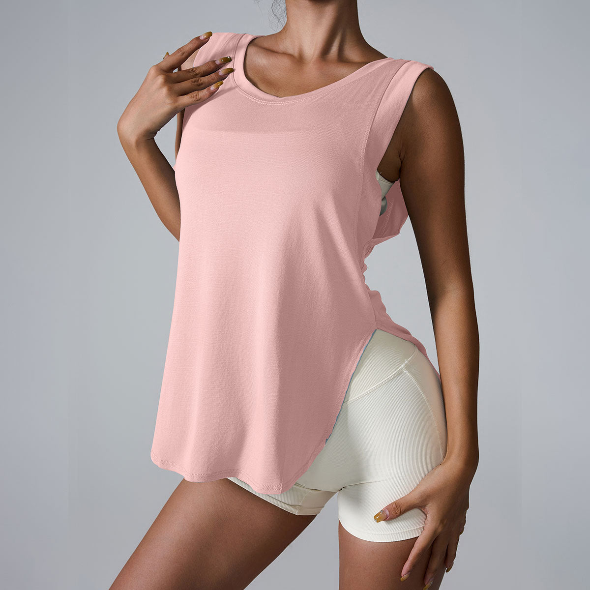 A woman is wearing a blush pink sleeveless tank with rounded hem, paired with ivory shorts, posing with hand on shoulder