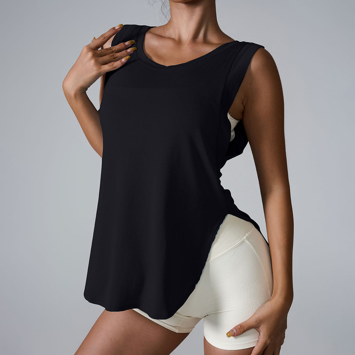 A woman is wearing a black sleeveless v-neck tank top with white athletic shorts, posing with one hand on her shoulder