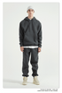 Male model with short hair wearing a charcoal gray sweatsuit with hoodie, white undershirt, and matching joggers