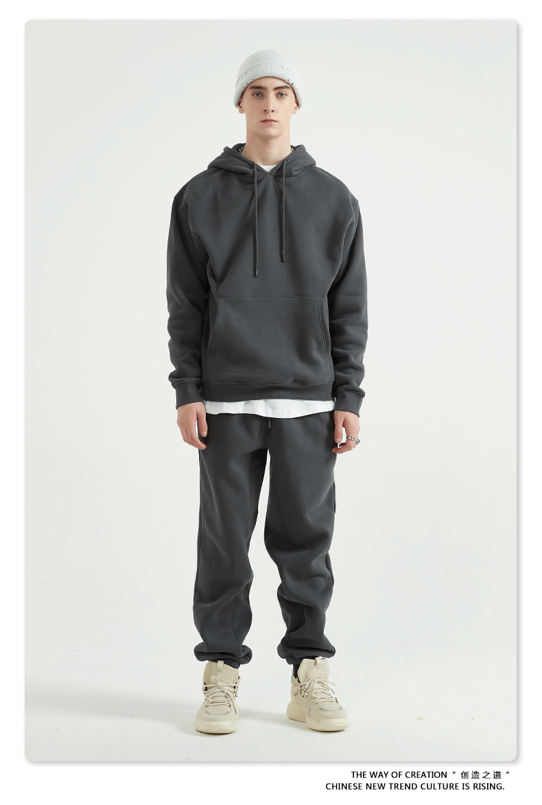 Male model with short hair wearing a charcoal gray sweatsuit with hoodie, white undershirt, and matching joggers