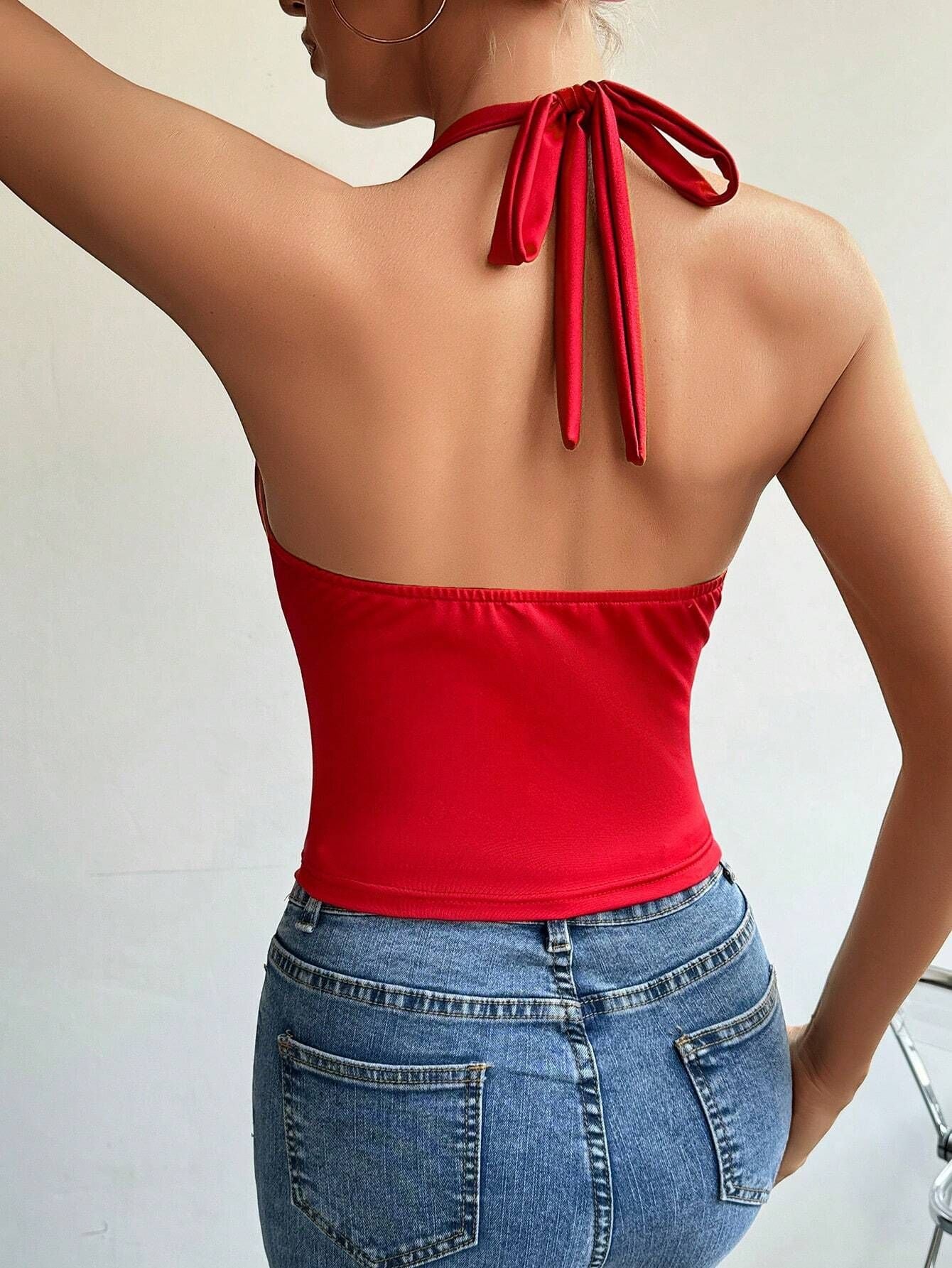 A woman is shown from behind wearing a red tie-neck bodysuit with an open back design and ribbon closure, paired with blue denim jeans