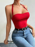 A woman is sitting on a transparent chair wearing a red halter bodysuit with bandeau-style top, paired with blue jeans and a black leather belt with decorative buckle