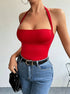 A woman is posing in a vibrant red halter neck bodysuit with a bandeau top, paired with blue denim jeans and a black belt with gold buckle against