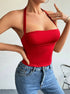 A woman is posing with one hand raised wearing a scarlet red halter bodysuit with structured bust, styled with blue denim jeans and delicate gold jewelry