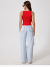 Back view of model wearing red crop top and wide-leg jeans, black sunglasses and hoop earrings against white backdrop