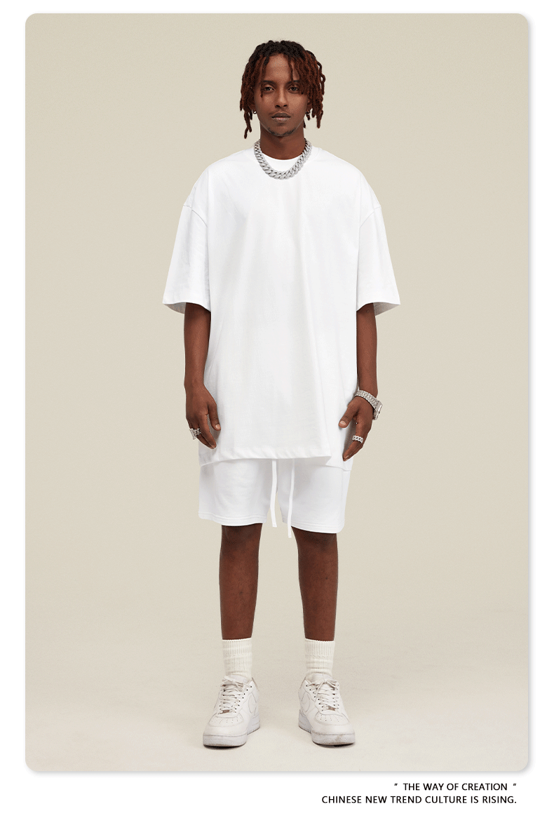 Man wearing white oversized T-shirt and shorts set with silver chain necklace and white sneakers