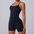 A model wearing black spandex one-piece bodysuit with thin straps and built-in shorts against neutral background