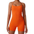 A model wearing bright orange form-fitting bodysuit with scoop neckline and compression shorts against light background