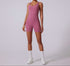 Model in mauve pink sleeveless bodysuit with scoop neckline and bike short length, paired with white socks and sneakers