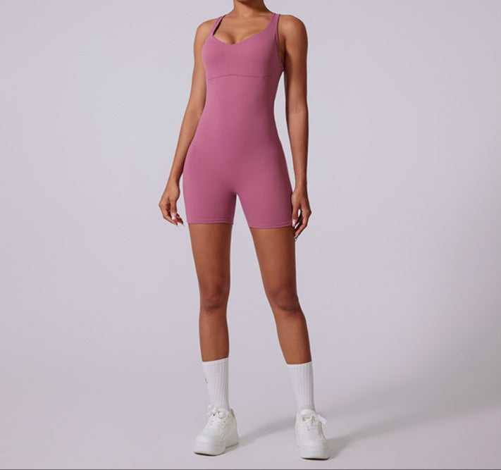 Model in mauve pink sleeveless bodysuit with scoop neckline and bike short length, paired with white socks and sneakers