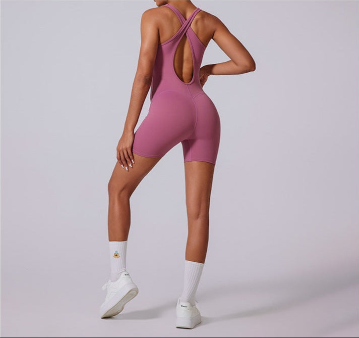 Back view of mauve pink bodysuit showing cross-back strap design and bike short length, styled with white socks and sneakers