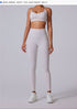 Full-body view of a woman in white high-waisted athletic leggings with a white sports bra and white sneakers, standing against a gray background