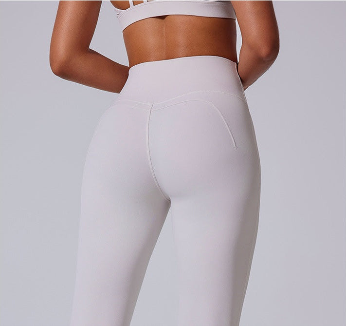 A woman wearing white high-waisted athletic leggings with a matching white sports bra, photographed from behind against a gray background