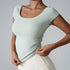Model demonstrating stretch in mint green fitted workout top with ruched sides and cream leggings against neutral backdrop