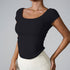 Model in black square-neck fitted crop top with puff sleeves and cream leggings against minimalist gray backdrop