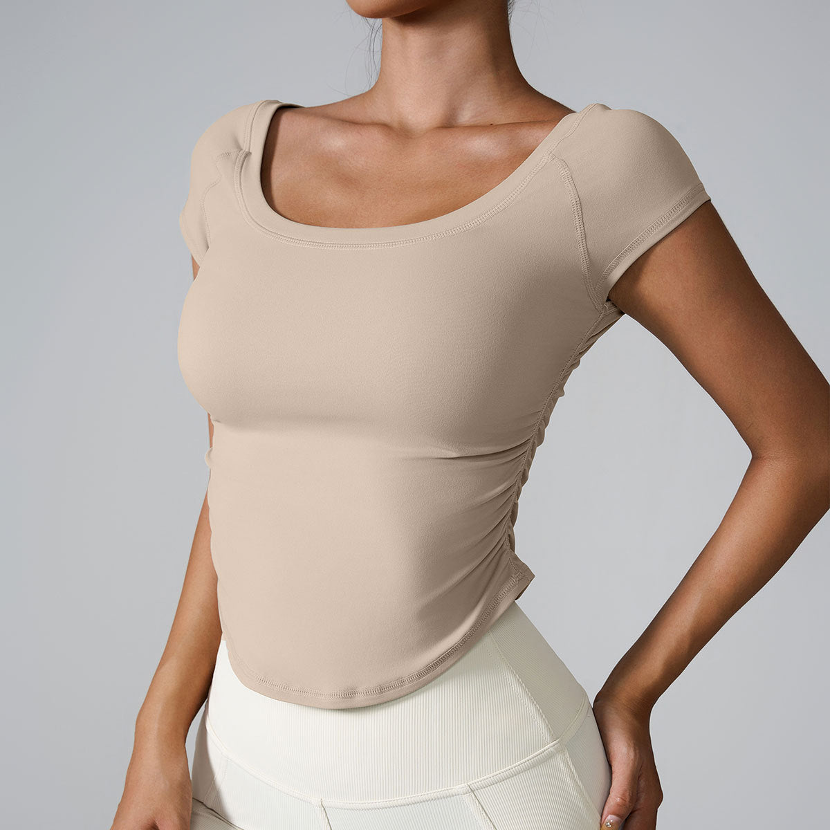 Model wearing nude square-neck crop top with side ruching and cream leggings, photographed against gray background