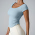Model in powder blue square-neck fitted top with ruched sides and cream leggings against neutral gray backdrop