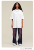 Woman wearing oversized white t-shirt with purple distressed wide-leg jeans and white sneakers against neutral backdrop
