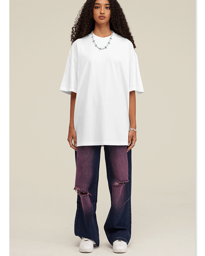 Woman wearing oversized white t-shirt with purple distressed wide-leg jeans and white sneakers against neutral backdrop