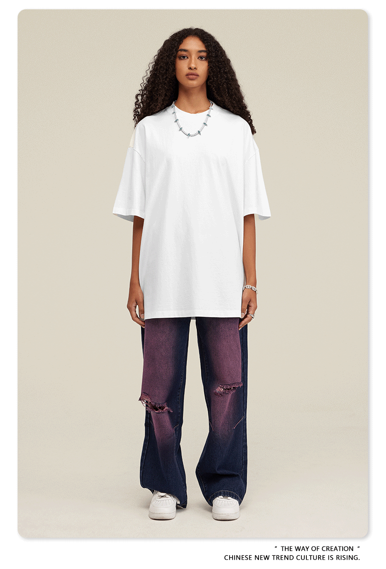 Woman wearing oversized white t-shirt with purple distressed wide-leg jeans and white sneakers against neutral backdrop