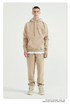 Male model with short hair wearing beige sweatsuit set with matching hoodie and pants, styled with beige sneakers