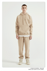 Male model with short hair wearing a beige sweatsuit with hoodie, white undershirt, and matching joggers