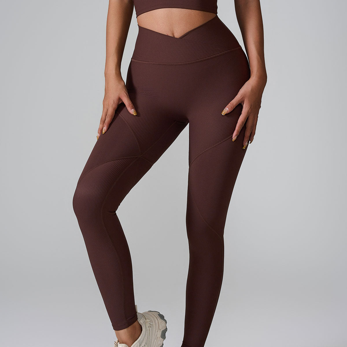 A model wearing brown ribbed workout leggings with V-waistband and matching top against gray backdrop