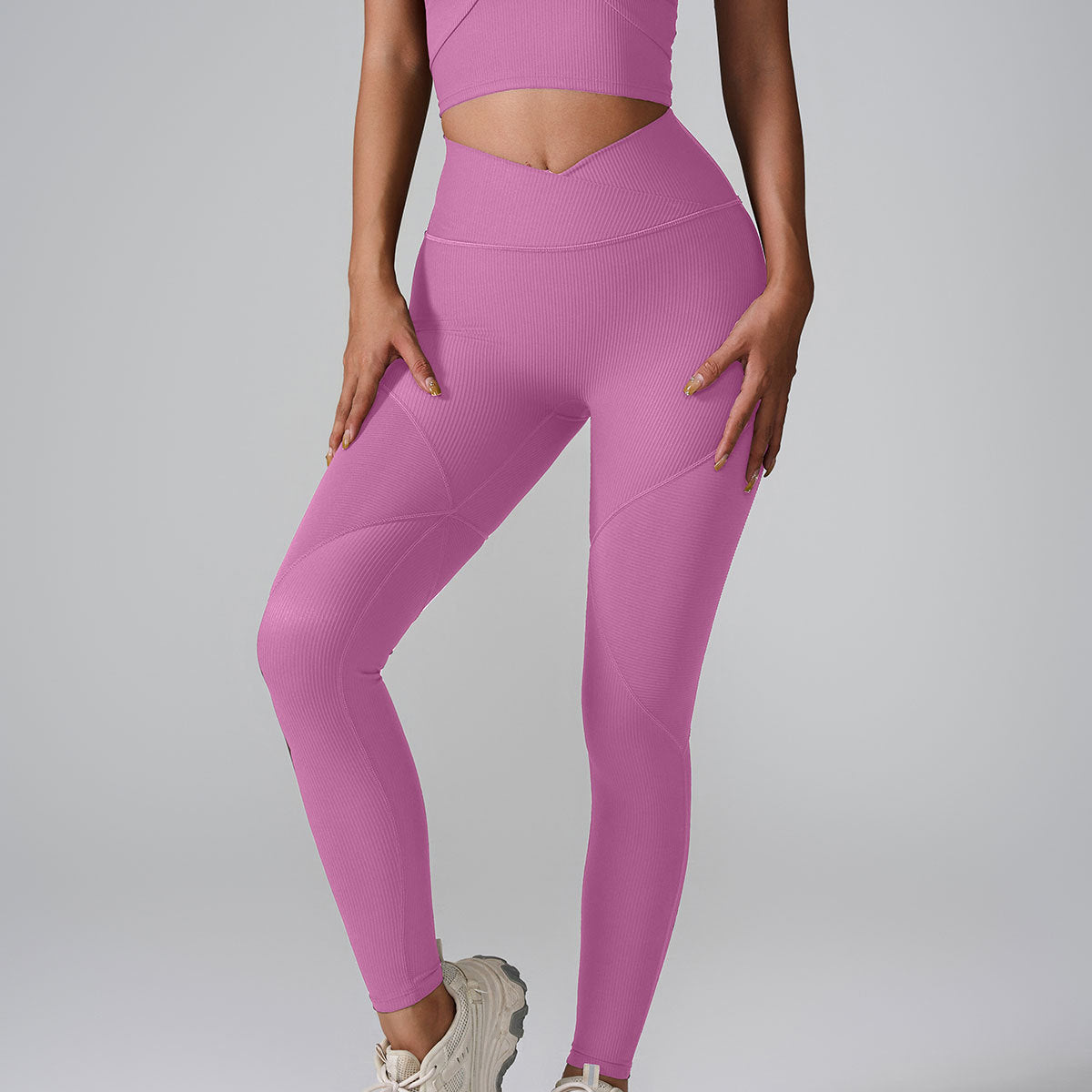 A model wearing lilac ribbed leggings with V-shaped waistband and matching crop top against gray background