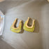 Gold-tone geometric hoop earrings with yellow-green translucent panels displayed on gray fabric surface, showing modern jewelry design