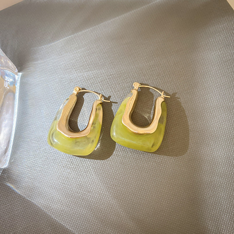 Gold-tone geometric hoop earrings with yellow-green translucent panels displayed on gray fabric surface, showing modern jewelry design