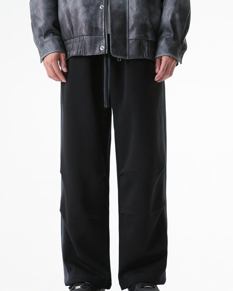 Black wide-leg drawstring pants displayed on a model wearing a gray leather jacket and black sneakers