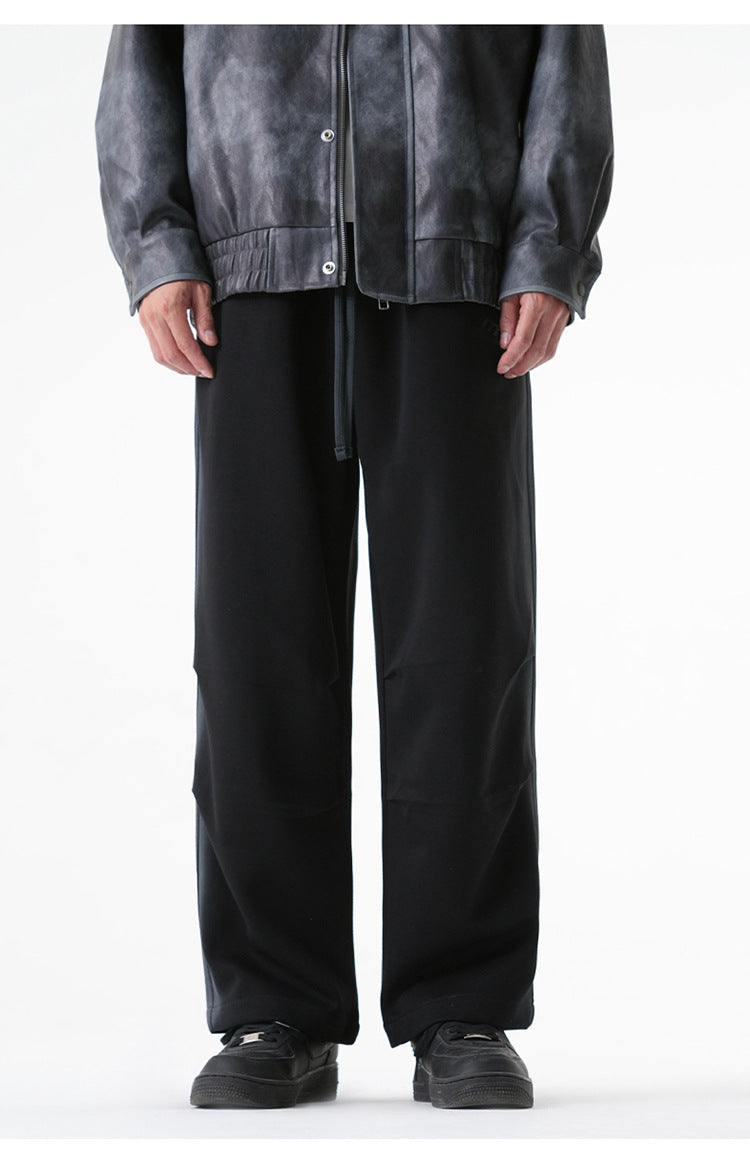 Black wide-leg drawstring pants displayed on a model wearing a gray leather jacket and black sneakers