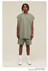 Male model wearing sage green sleeveless top and matching shorts with silver jewelry and white sneakers