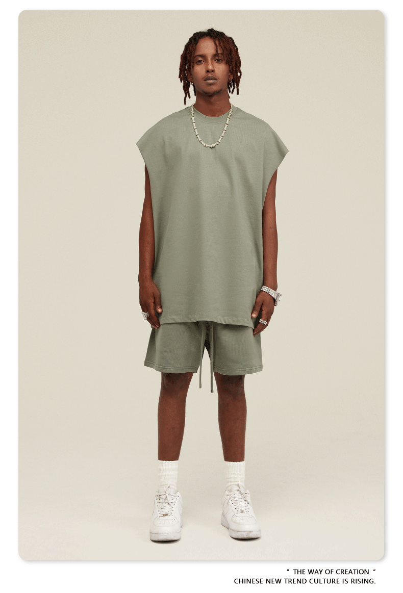Male model wearing sage green sleeveless top and matching shorts with silver jewelry and white sneakers