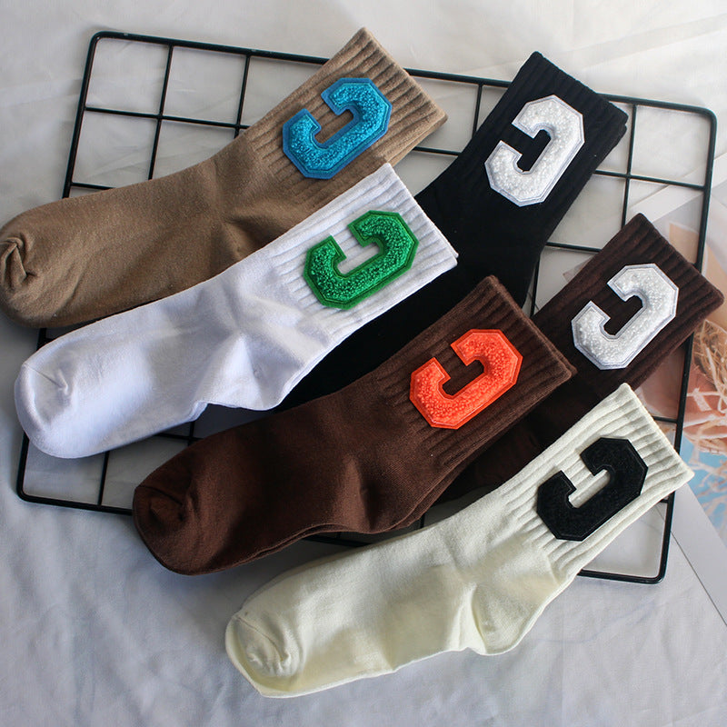 Six pairs of varsity-style crew socks in beige, white, brown, black, and cream, each featuring a bold "C" patch in different colors