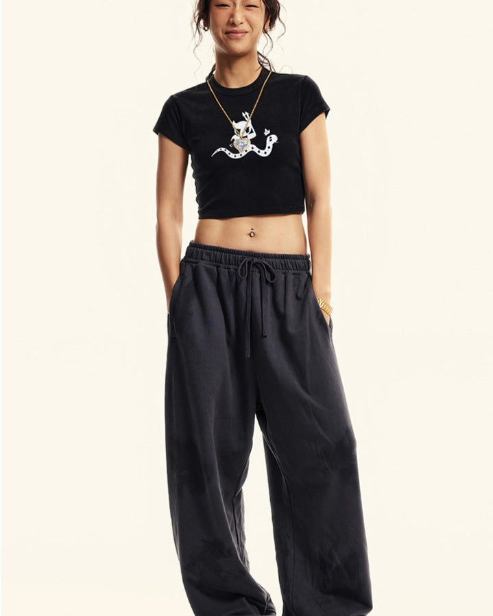 Full-body shot of a model wearing a black cropped graphic t-shirt and oversized black sweatpants