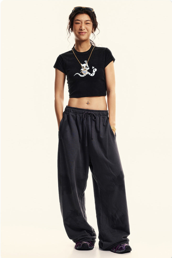 Full-body shot of a model wearing a black cropped graphic t-shirt and oversized black sweatpants