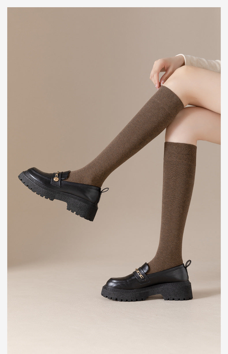 Close-up of legs in brown knee-socks and black chunky loafers in seated position
