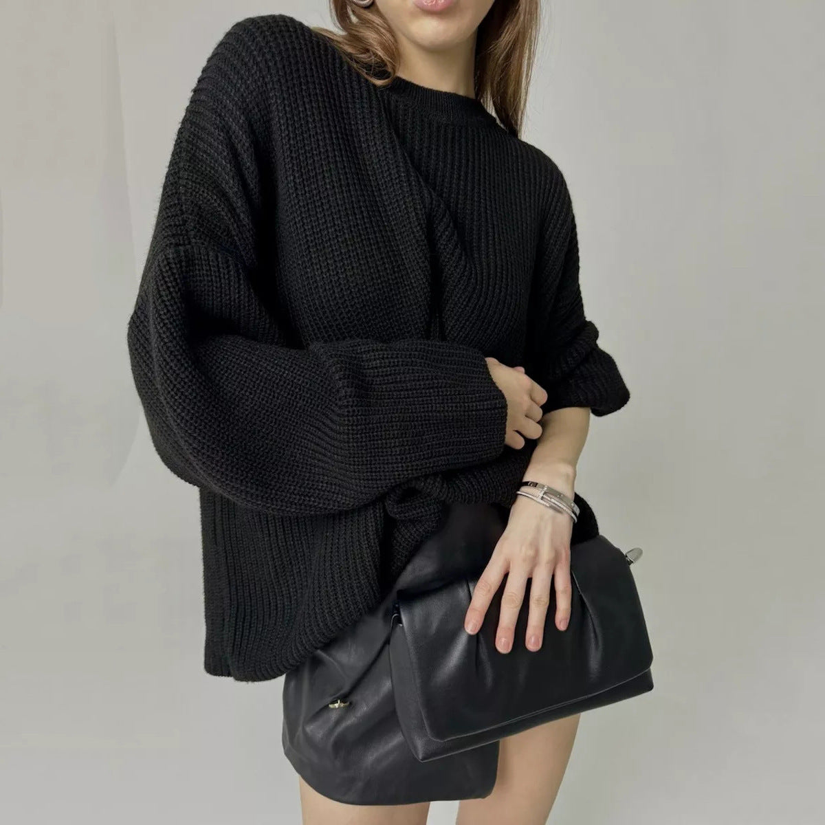 Oversized black ribbed knit sweater paired with leather pants and black handbag, model shown from torso down