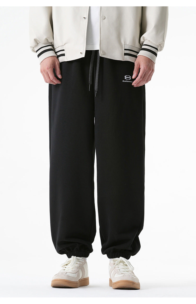 A close-up of black jogger sweatpants featuring a drawstring waist, elastic cuffs, and a small embroidered logo on the left thigh