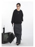 Black snap-detail hoodie with curved seam design, shown with floor-length gray skirt and chain-strap handbag